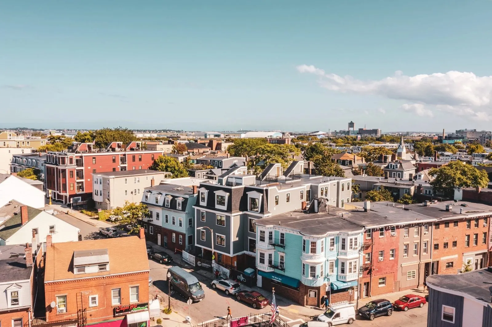 Drone view over East Boston triple-deckers — one of Ethan's projects mid-build, Boston skyline on the horizon